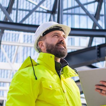 Construction site manager in a white hard hat and hi-vis jacket, holding a tablet