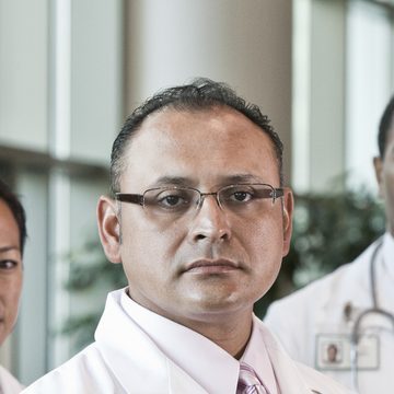 Healthcare professional in a white coat with colleagues behind him
