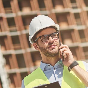 Tradesperson in a hard hat and hi-vis vest taking a phone call on site